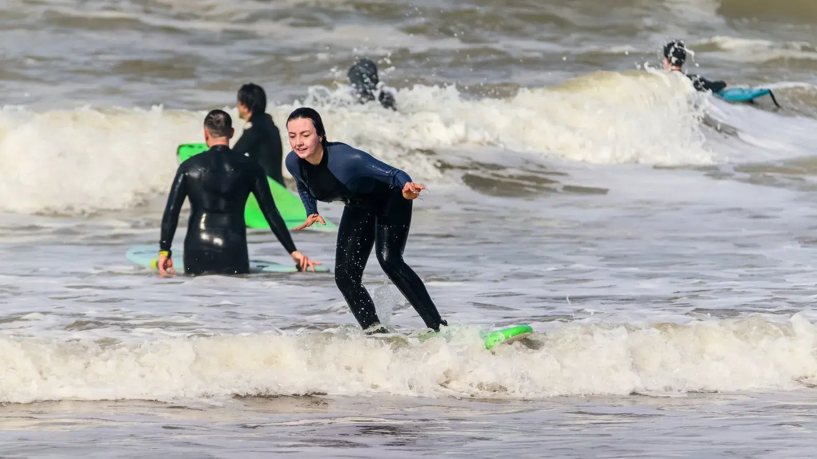 First waves in the whitewater off Mirleft: a beginner stands up on the soft board, the group waiting behind her.